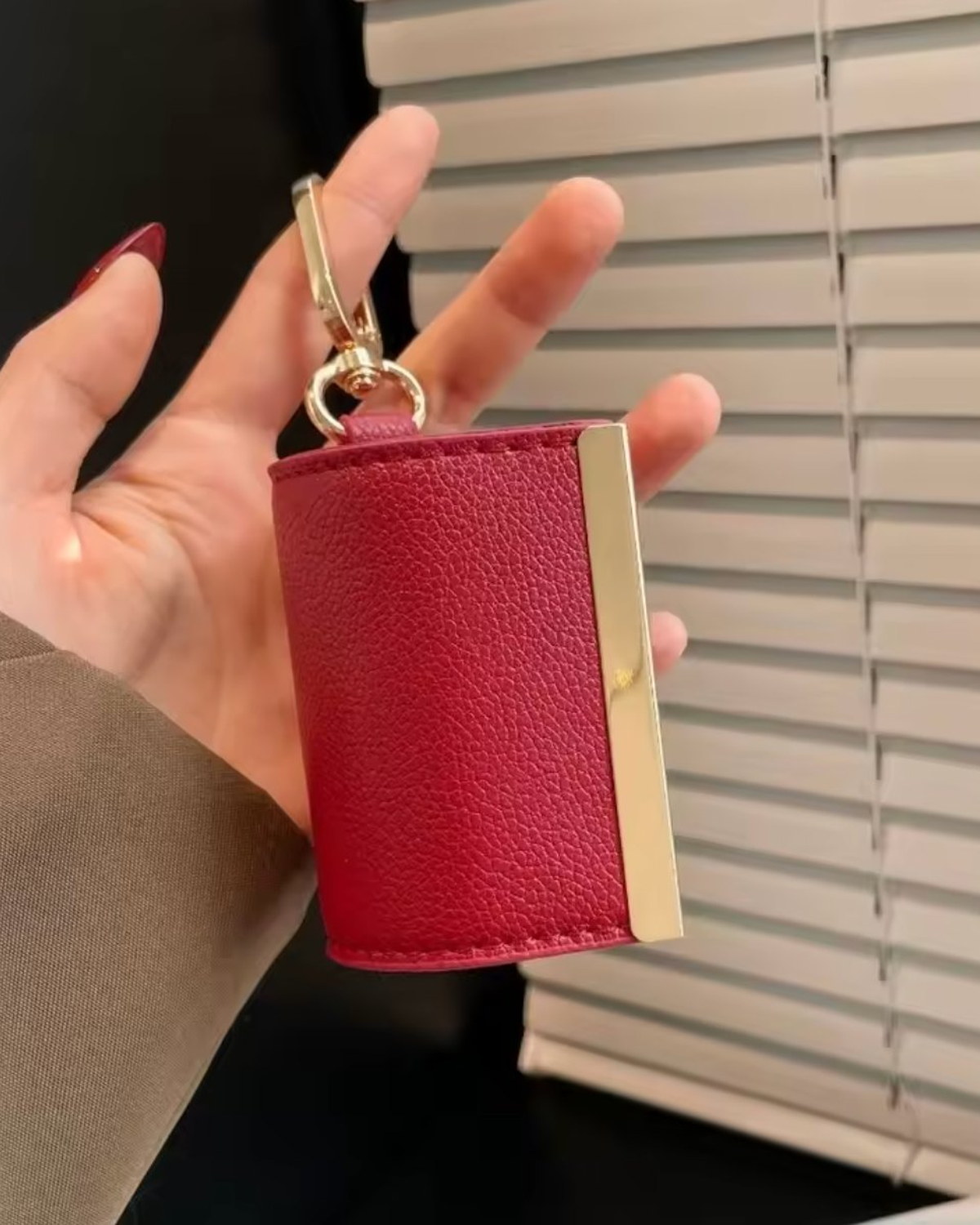 Main tenant la pochette TOTEGO fermée, cuir grainé rouge et barre dorée avec mousqueton